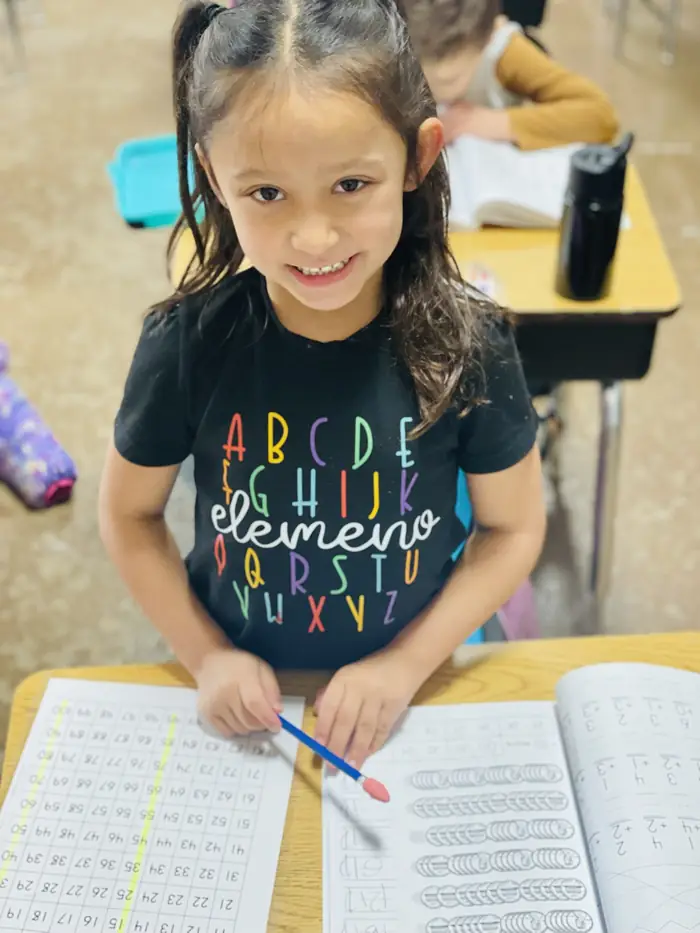 A Cornerstone student smiling up from her math workbook and hundreds chart