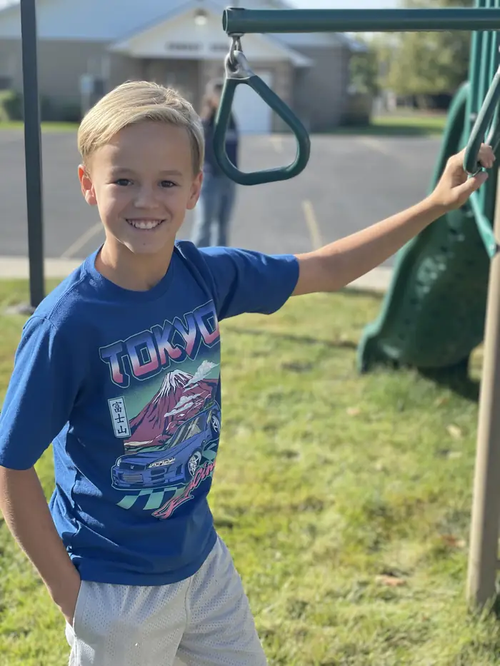 A Cornerstone student smiling beside the playground rings with the school building behind him