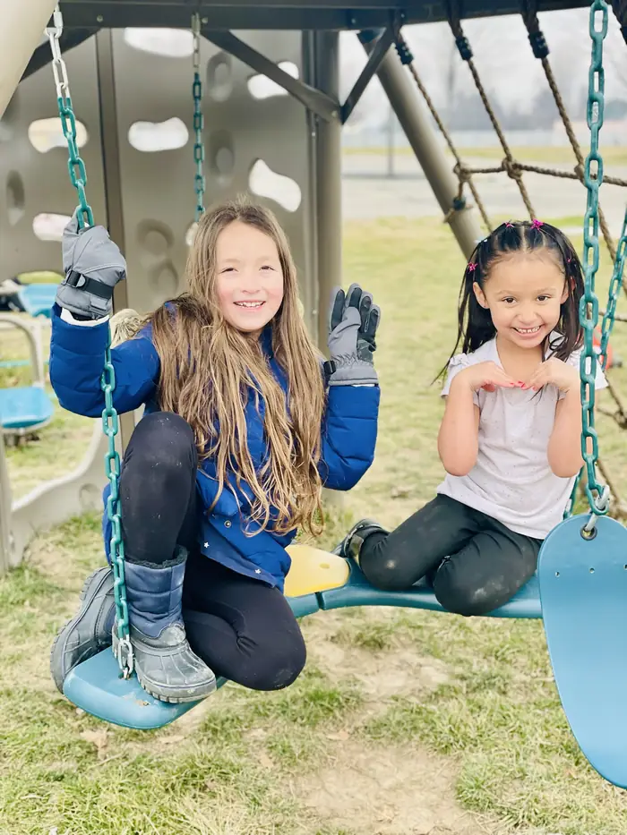 Two Cornerstone students smiling and waving from the playground swings